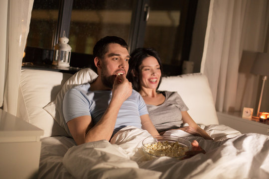 couple with popcorn watching tv at night at home