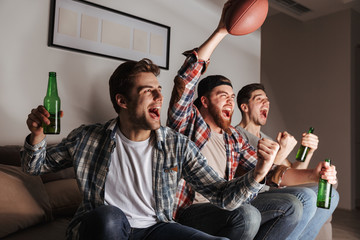 Handsome satisfied bachelors shouting happily while partying at home, and watching football play...