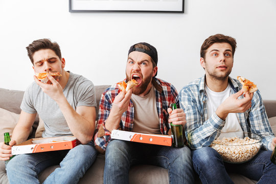 Image of young bachelors eating pizza while resting at home, and watching football game