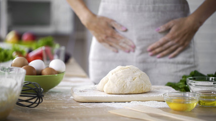 Dough on kitchen table with woman in apron standing behind, biscuit cooking