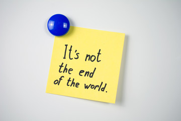 yellow sticker inscription It's not the end of the world attached  blue magnet  white fridge. close-up