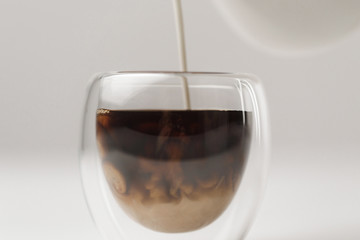 Pouring milk to cup with coffee on white background