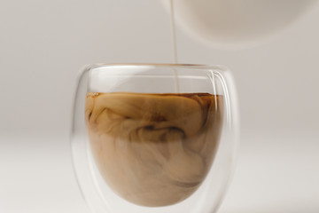 Adding milk to cup with coffee on white background