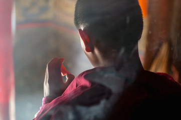 Child buddhist monk praying in monastery, shot from behind, close-up, Tibet