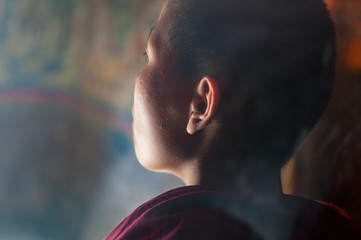 Child buddhist monk praying in monastery, shot from behind, close-up, Tibet