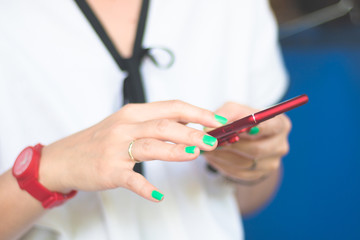 asian woman with white blouse hold red smartphone with left hand and touch screen with right fingers in golden light, red watch on right wrist, green nail polished