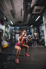 Obraz na płótnie Canvas Gorgeous attractive motivated girl doing squats with kettlebell in the gym.