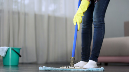 Housewife carefully washing floor in her apartment with mop, spring-cleaning