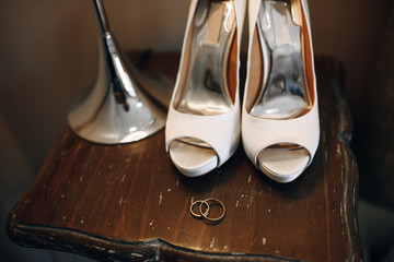 Bride's shoes on the wooden chair, wedding rings and torchere near