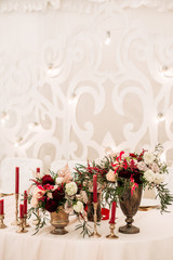 Decorate table with white tablecloth, red bouquets with fern and eucalyptus in brass vases, red candles near