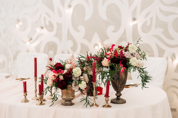 Decorate table with white tablecloth, red bouquets with fern and eucalyptus in brass vases, red candles near