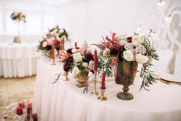 Decorate table with white tablecloth, red bouquets with fern and eucalyptus in brass vases