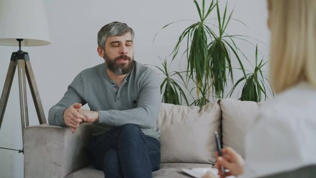Adult bearded man talking about his problems to psychologist in her office indoors