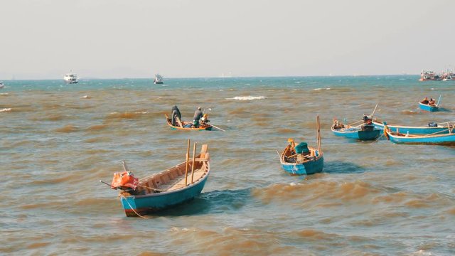 Small fishing boats sail along the lush sea on waves. Fishermen catch fish in the sea