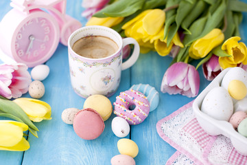 Spring morning, fragrant coffee and tulips of yellow and pink color. Donuttsy copies. Blue wooden background, place for text and postcard.