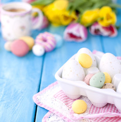 Breakfast in the spring morning. Yellow and pink tulips. A refrigerator. A coffee in a beautiful mug. Same eggs. Pascha. A dining room napkin. A blue wooden background. An opening and text.