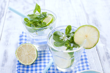 Two glasses of water and fresh green mint, and lime. On a blue napkin on a wooden background. free space for text or a postcard.