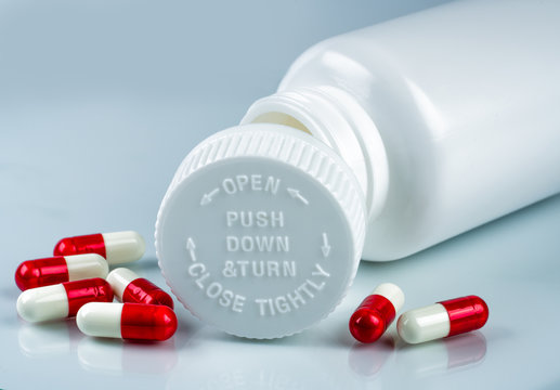 Capsules pills on white background and plastic bottle with blank label and copy space. Childproof packaging. Child resistant pill container. Push down and turn cap.Global healthcare and love concept.