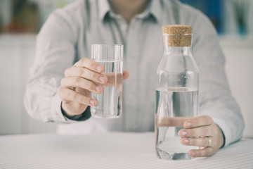 Young man having glass of water and holding bottle in kitchen