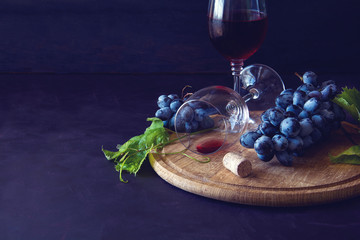 Two wineglasses with red wine and grapes decorated vine leaves on dark wooden desk. Toned