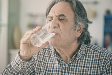 Naklejka na ściany i meble Senior man drinking water from glass in kitchen