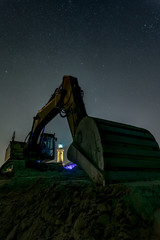 Silhouette of an excavator in front of the landmark Leuchtturm Warnem&uuml;nde at night. Concept: maritime or vacation and travel