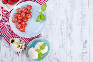 Traditional Italian salad with fresh cherry tomatoes and soft mazarella cheese, with basil and olive oil. Ingredients for salad. Portions in plates. Free space for text.