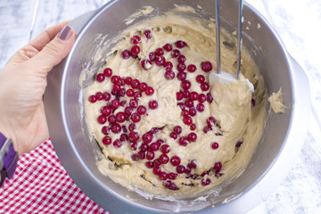 Red berries in a dough for a home-made pie. In a steel bowl. White wooden background and free space for text.
