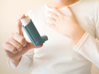 Young female in white t-shirt using blue asthma inhaler for relief asthma attack. Pharmaceutical products is used to prevent and treat wheezing and shortness of breath caused asthma or COPD. Close up. - obrazy, fototapety, plakaty
