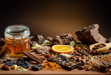 Still life with a set of chocolate, nuts, spices, honey, raisins, cocoa, orange peel on a wooden table, close-up