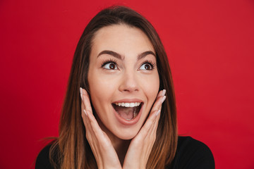 Portrait of amazing woman 20s raising arms to face and expressing surprise, isolated over red background