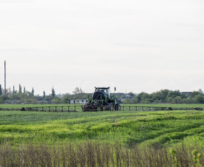 Fototapeta premium Tractor with a spray device for finely dispersed fertilizer. Tractor on the sunset background. Tractor with high wheels is making fertilizer on young wheat. The use of finely dispersed spray chemicals