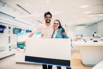 Happy young lovely modern couple with bought big tv in the electronic store.