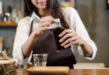Asian Barista woman Cold brew coffee in glass bottle to a cup glass in the coffee shop. people with barista in cafe concept.