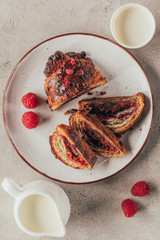 flat lay with arranged jug and cup of milk and sweet pastry with raspberries on plate on light tabletop