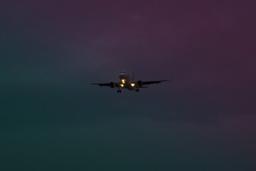 Fototapeta na wymiar A plane taking off at dusk amid a surreal purple blue and green sky