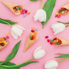 Pattern of colorful bright candy in waffle cones and white flowers on pink background. Flat lay, top view