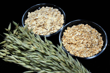 Oat ears and oatmeal flakes on black background