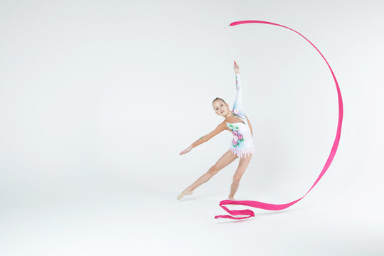 Rhythmic gymnastics caucasian blonde girl in dress for show performing athlete exercises with pink ribbon handling abilities showing flexibility and acrobat balance on white background isolated