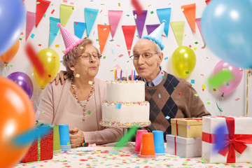 Senior couple blowing candles on a birthday cake