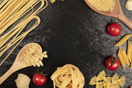 Overhead photo of different types of pasta with cherry tomatoes on black