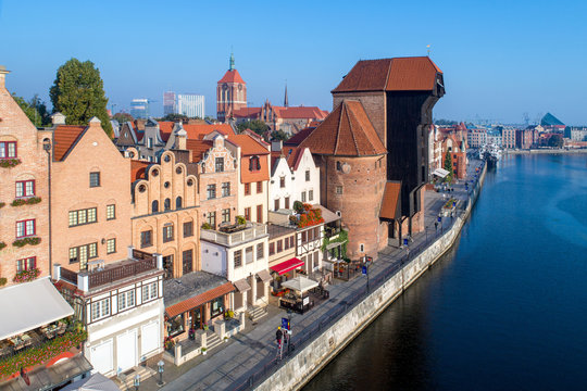 Gdansk old city in Poland with the oldest medieval port crane (Zuraw) in Europe, St John church and Motlawa River with embankment and promenade. Aerial view in early morning. Sunrise light.