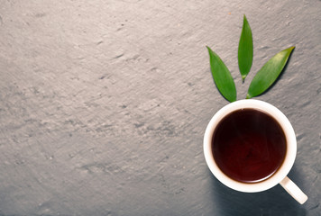 Detox tea concept, white cup on dark grey chalk board with green leaves, herbal tea  natural coffee, hot organic healthy purifying drink,  copy space for text, top view 