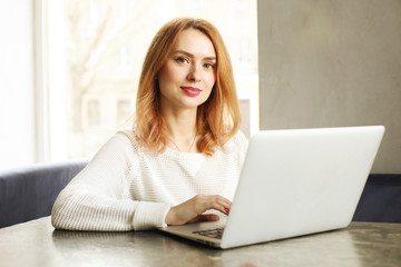 Fototapeta premium Attractive hipster young woman in modern loft cafe coffee shop restaurant. Writer, blogger, designer, freelancer, remote work process. E-shopping, online shopping, m-shopping.
