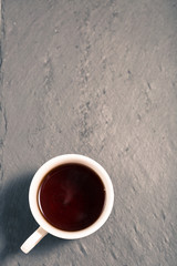 Detox tea concept, white cup on dark grey chalk board with green leaves, herbal tea  natural coffee, hot organic healthy purifying drink,  copy space for text, top view 