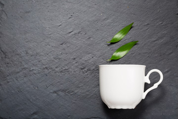 Detox tea concept, white cup on dark grey chalk board with green leaves, herbal tea  natural coffee, hot organic healthy purifying drink,  copy space for text, top view 