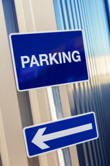 blue sign with white lettering - "Parking" and showing a left pointing arrow.