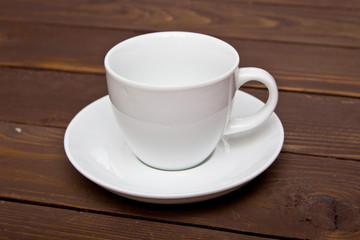 Empty white Cup with saucer on a wooden background, top view . Crockery for coffee and tea . Template for advertising and multimedia.