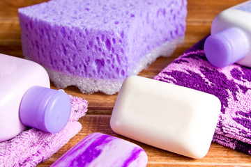 Obraz na płótnie Canvas Purple sponges,a towel, soap, shampoo, body cream on wooden background. Bath accessories set in lavender color
