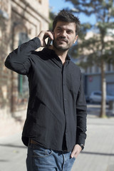 Young urban businessman on smart phone in street talking on smartphone smiling wearing black shirt